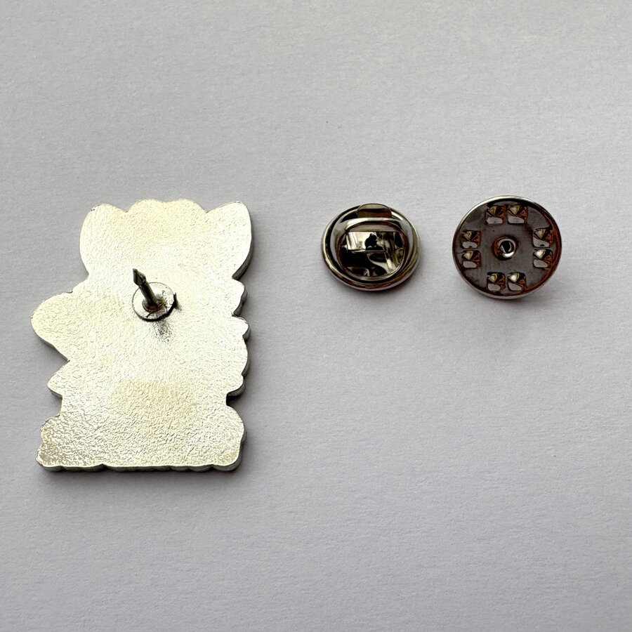 The back of an enamel pin showing its metal post, beside the separate butterfly clutch that locks it onto the backing card